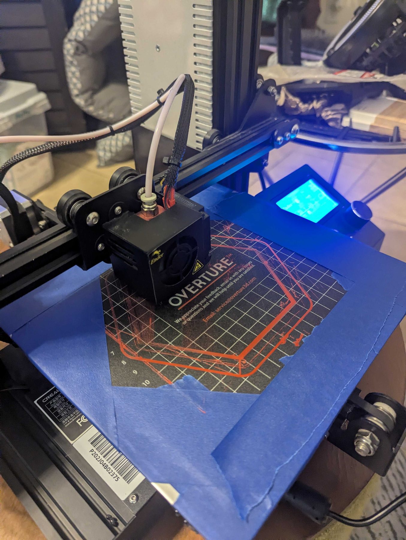 A 3D printer with its bed lit blue and a part-finished print in place.