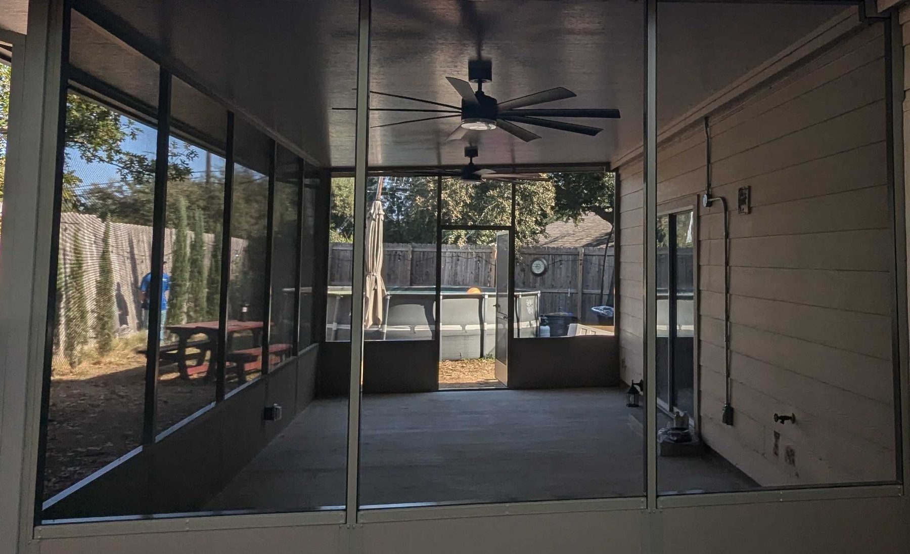 A screened porch built onto the back of a house, framed in mesh panels with a ceiling fan above.