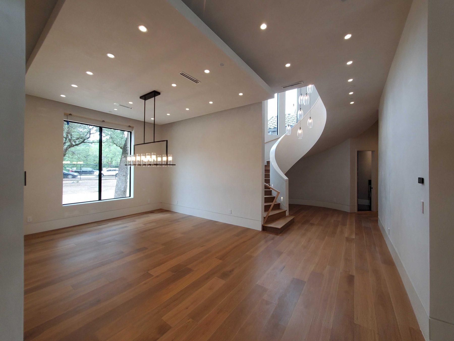 A large cleared room with wood floors, tall windows and a curved staircase, completely empty.