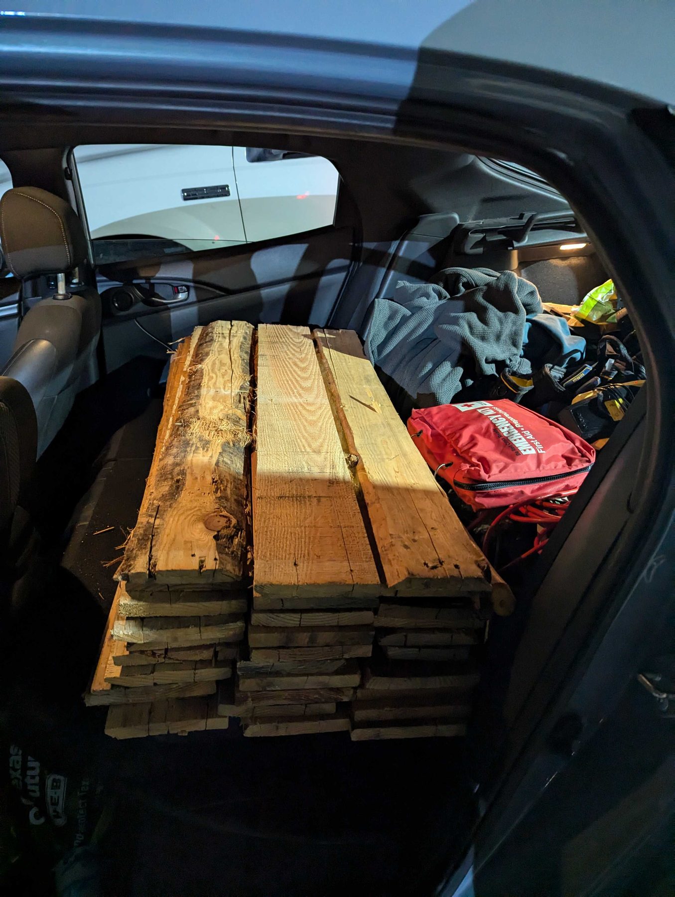 Reclaimed timber planks stacked into the back of a car, with tools and bags packed in around them.