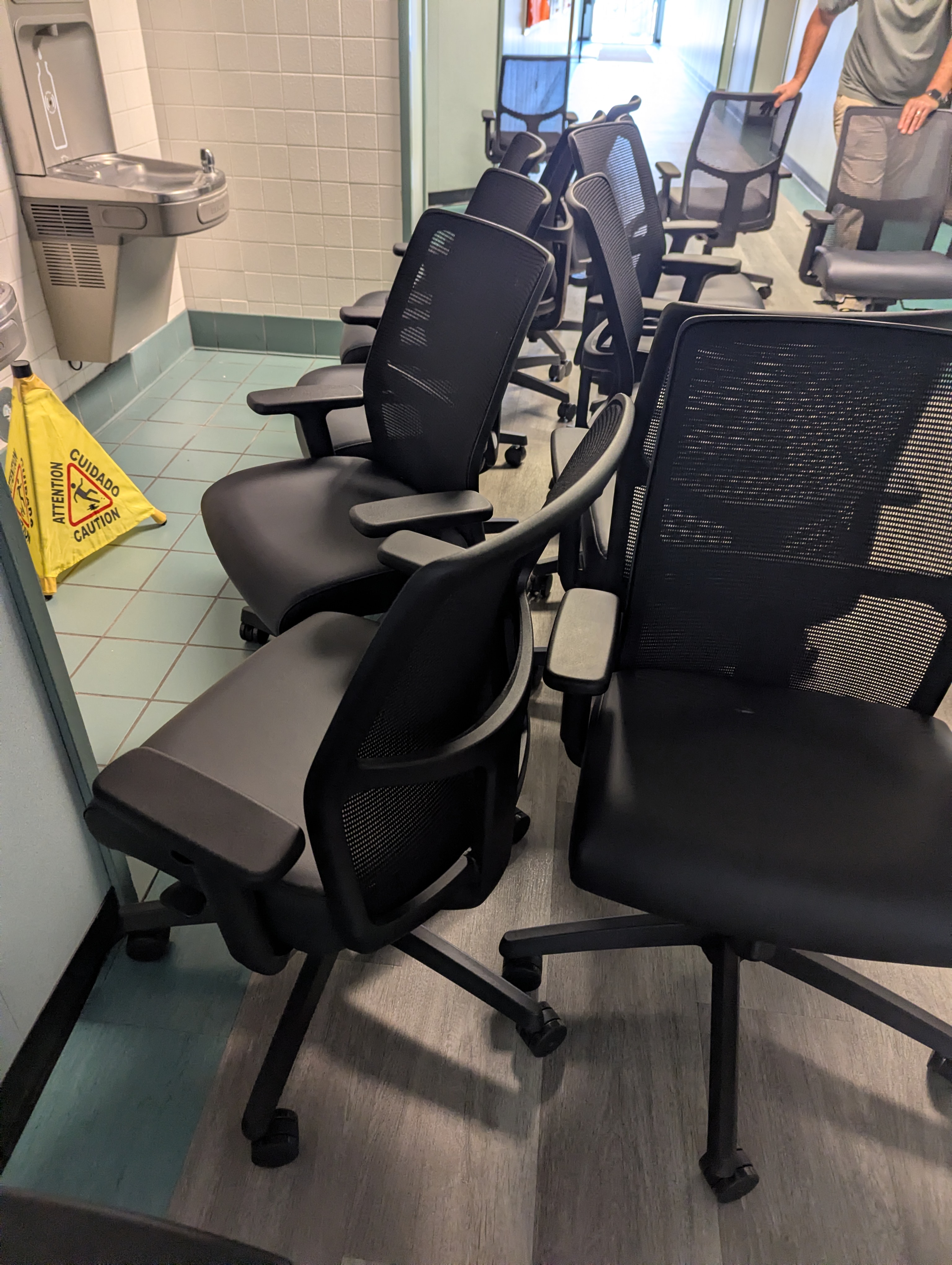 A row of new mesh back office chairs lined up along a school corridor, waiting to be distributed to rooms.