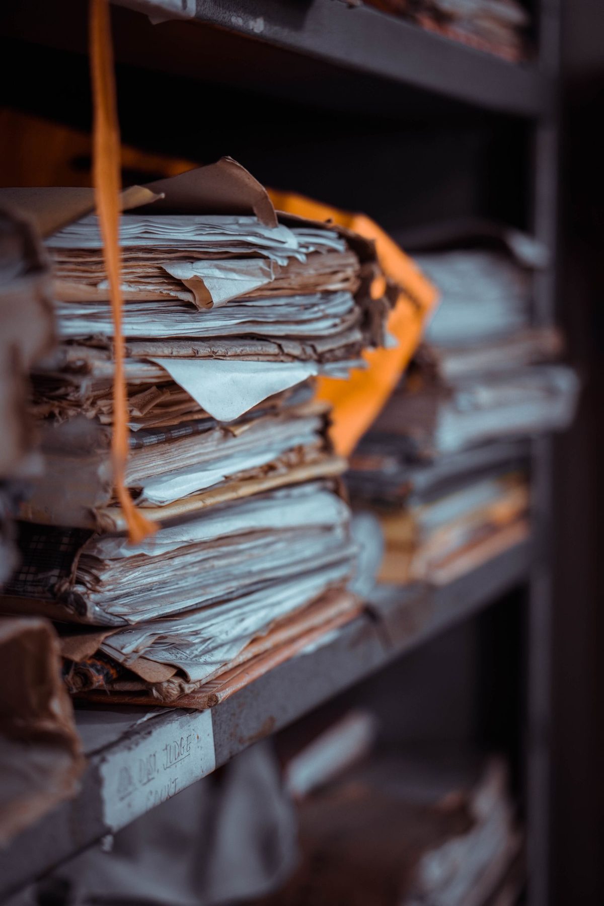 Stacks of tied paper files piled along a shelf, one bundle bound in an orange folder.