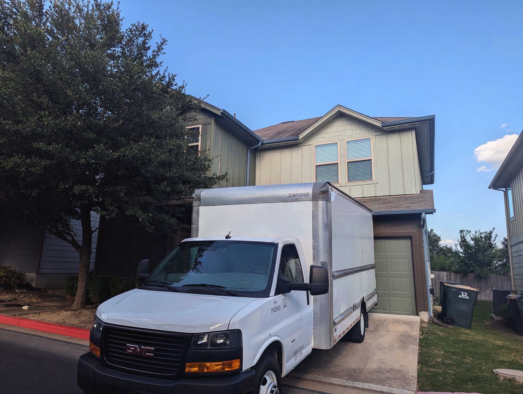 A white box truck parked at the curb outside a two-story house, with the garage standing open behind it.