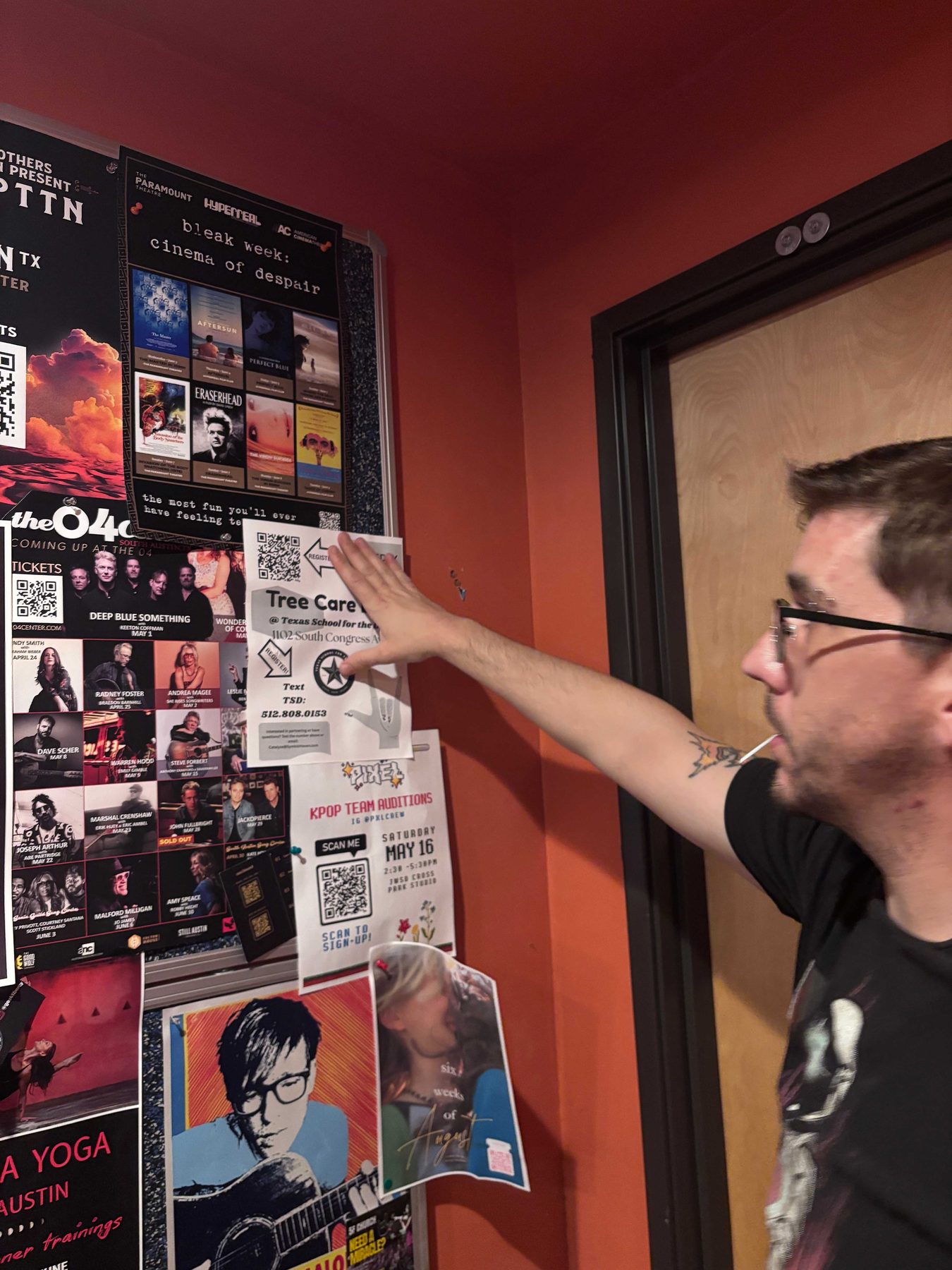 A wall densely covered in overlapping gig posters and flyers, with a person reaching up to add another one.