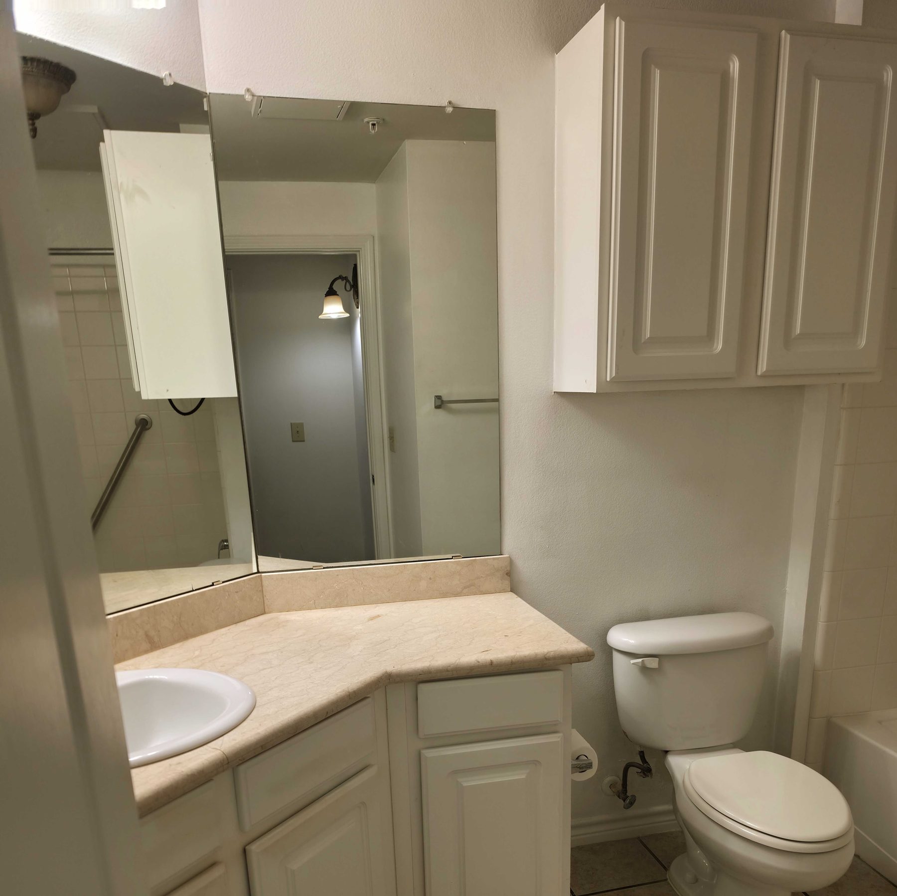 A cleaned bathroom with a bare counter, a wiped mirror and empty cabinets.