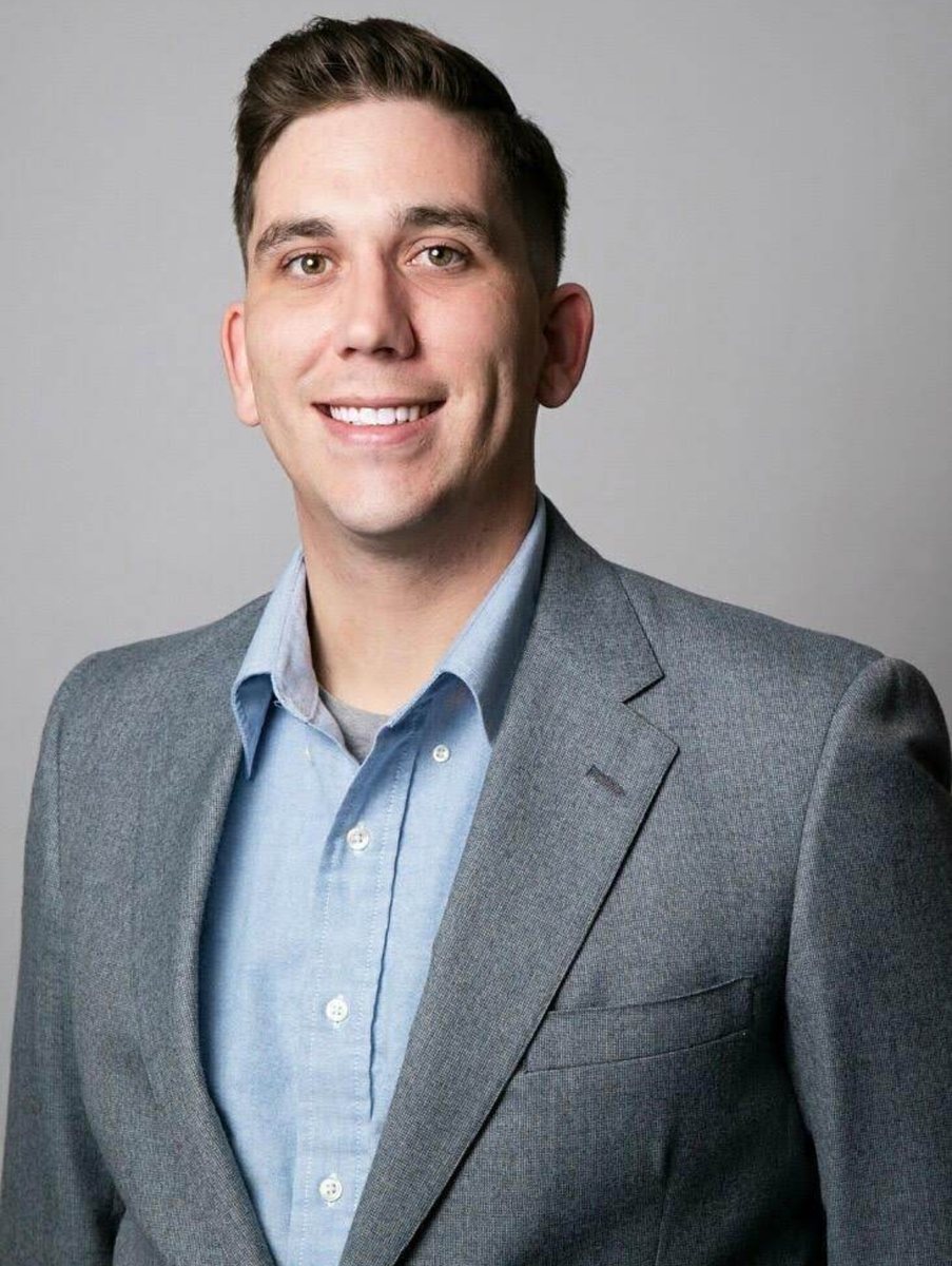 Brendon Wash in a gray jacket and blue shirt against a plain backdrop.