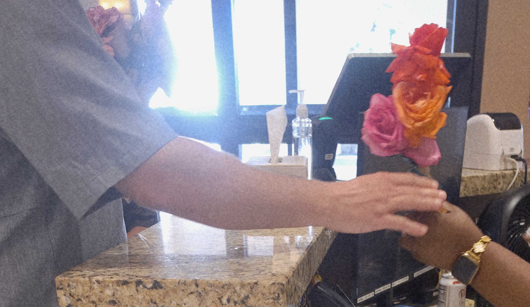 A posy of roses being handed across a front desk, one pair of hands passing it to another.
