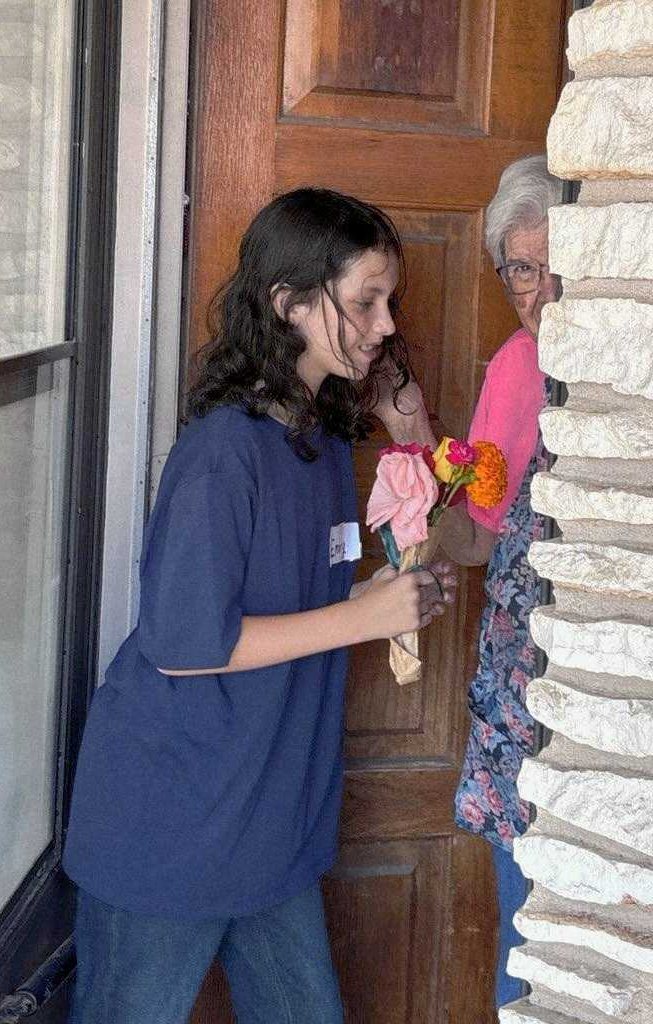 A child handing a small posy of roses and a marigold to her great grandmother at her front door.