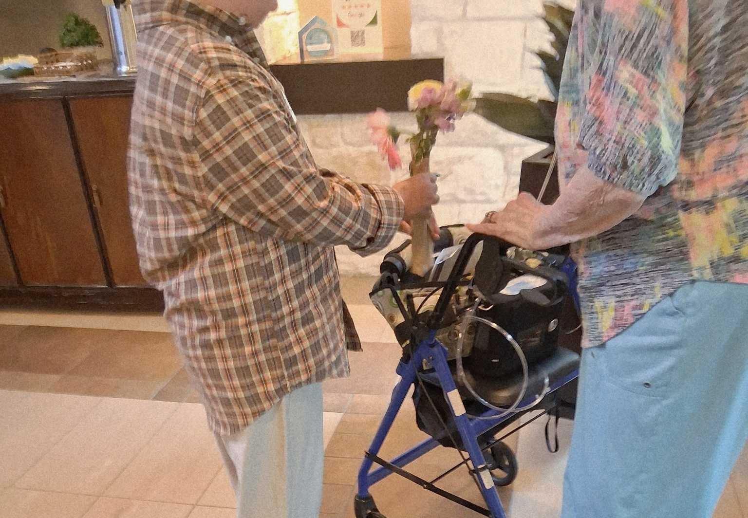 A posy in a jar being handed to a resident standing at their walker.