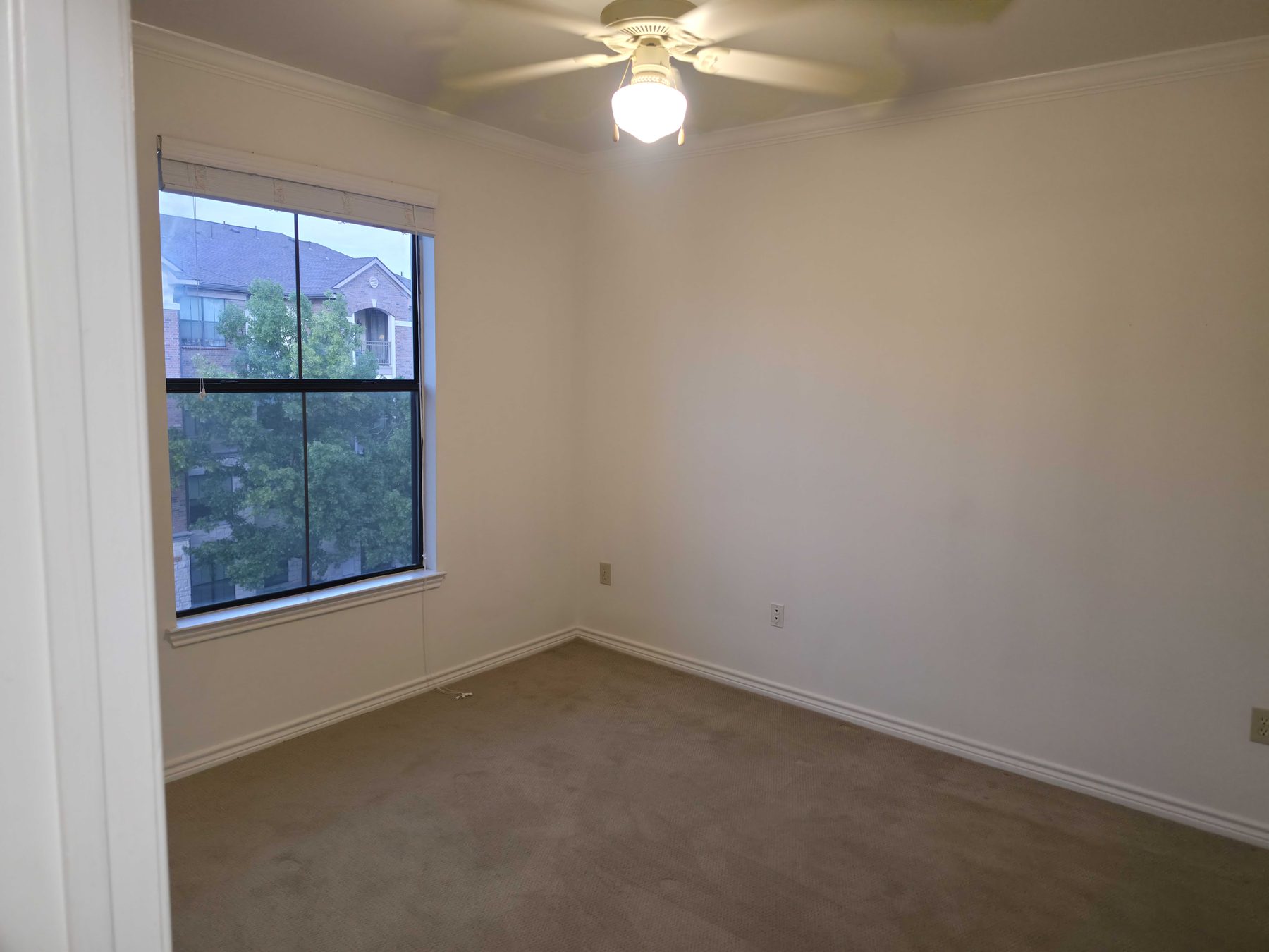 An emptied bedroom with bare carpet and the closet doors standing open.