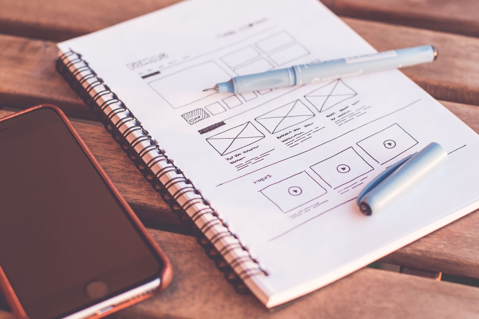 A page layout sketched by hand in a notebook, with a pen resting on it beside a phone.